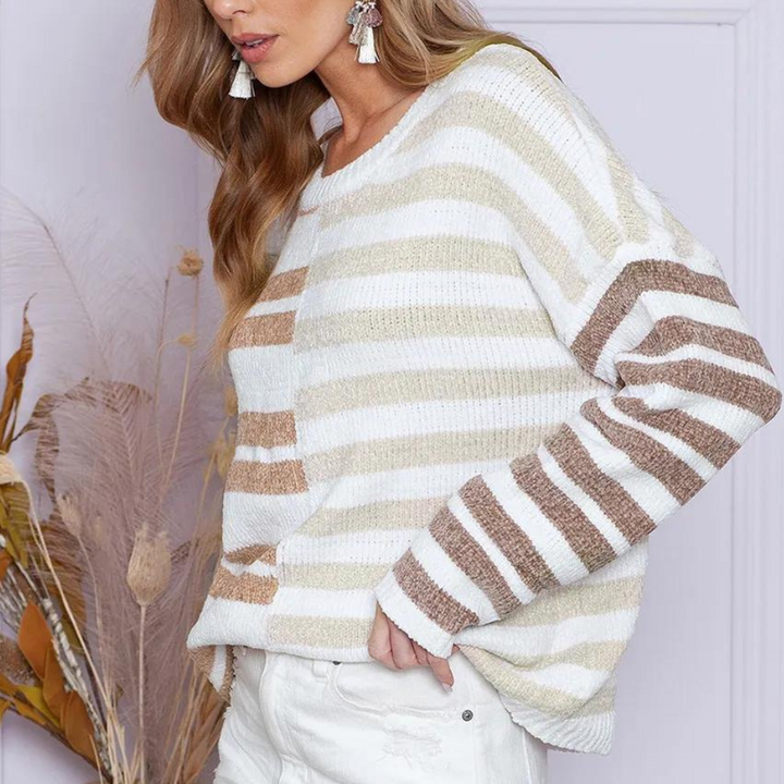 Vrouw draagt gebreide trui met beige en witte strepen, gecombineerd met witte jeans. Modieuze herfstoutfit, perfect voor casual en stijlvolle looks.