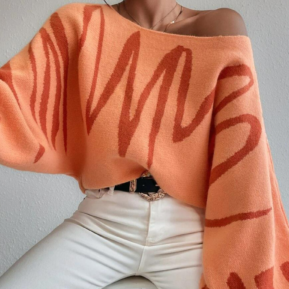 Oranje oversized trui met abstracte rode patronen, gedragen door model met witte broek. Trendy damesmode, herfstkleding, comfortabele stijl.