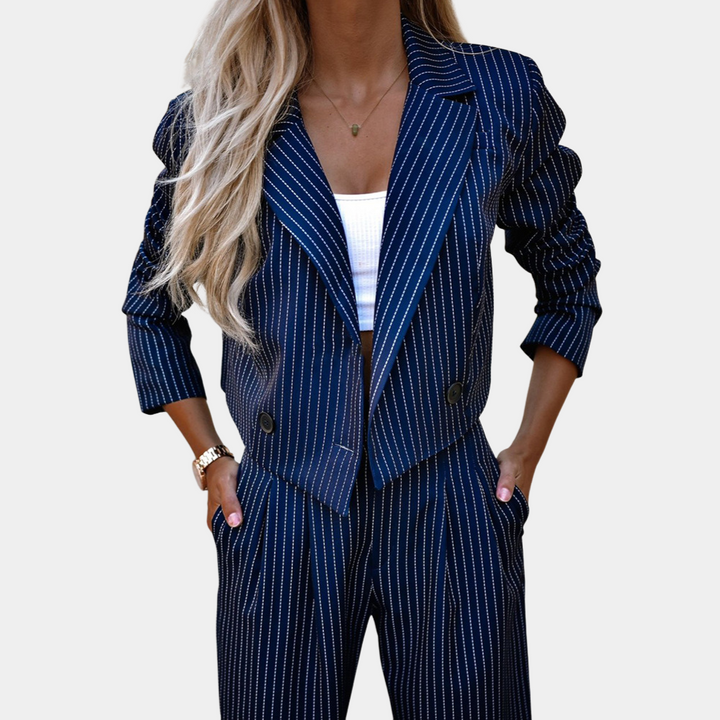 Vrouw in stijlvolle, gestreepte, donkerblauwe damespak met blazer en broek, witte top, lange blonde haren. Chique mode, zakelijke outfit.