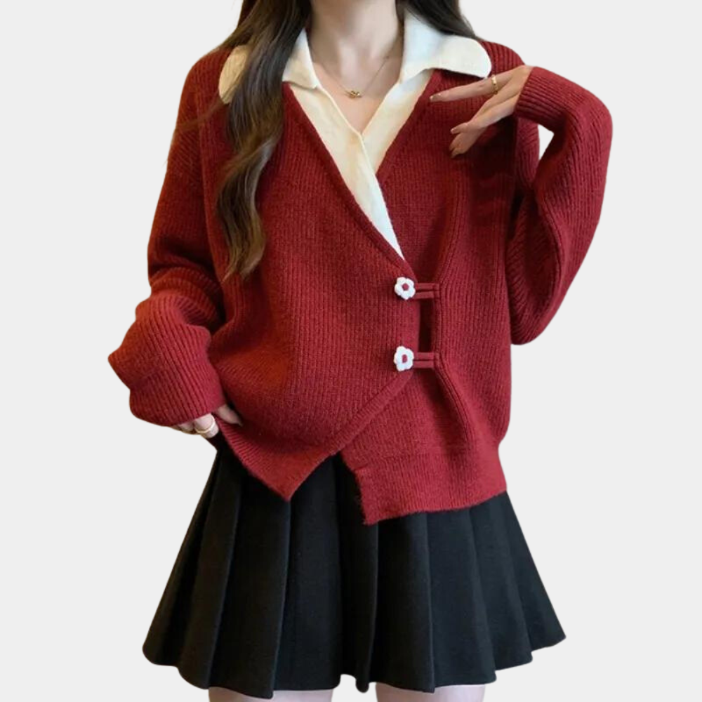 Rode oversized gebreide trui met bloemenknopen, gedragen over een witte blouse en zwarte plooirok. Modieuze dameskleding herfst/winter.