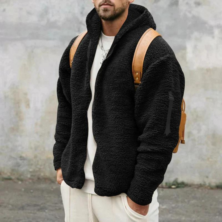 Man in zwarte fleece hoodie met capuchon, bruine rugzak, casual outfit. Warme herentrui, wintermode, comfortabele kleding.