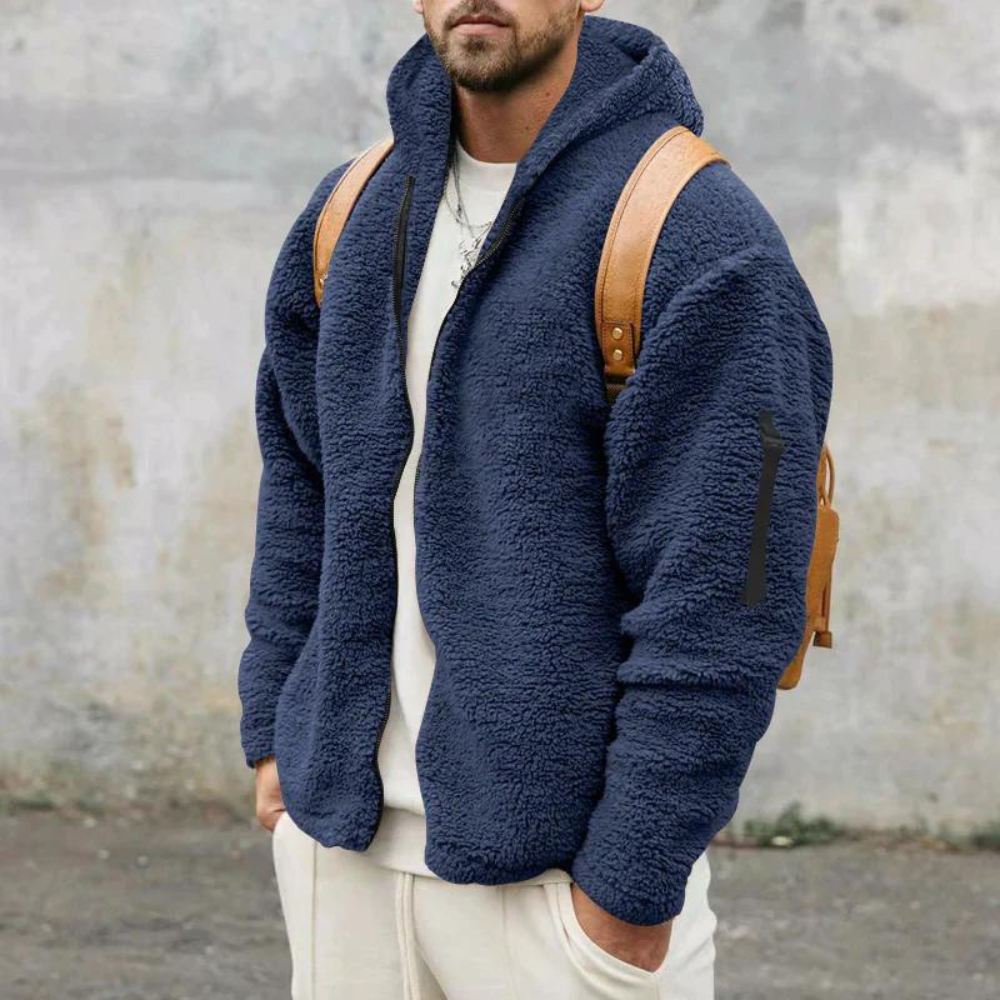 Man in blauwe fleece hoodie met capuchon, bruine rugzak, casual outfit, grijze achtergrond. Warme herentrui, comfortabele winterkleding.