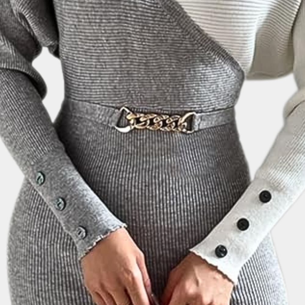 Grijze geribbelde trui-jurk met asymmetrisch ontwerp, metalen kettingriem en knoopdetails op de mouwen. Modieuze dameskleding, herfst/winter stijl.