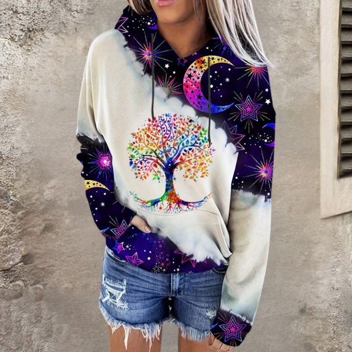 Vrouw draagt kleurrijke hoodie met boom- en sterrenprint, gecombineerd met denim shorts. Trendy mode, casual outfit, streetwear stijl.