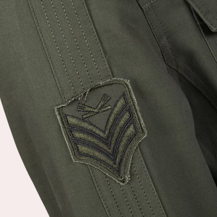 Olijfgroene militaire jas met zwart geborduurd embleem en chevrons op de mouw, detail van legerstijl kleding, duurzame mode.