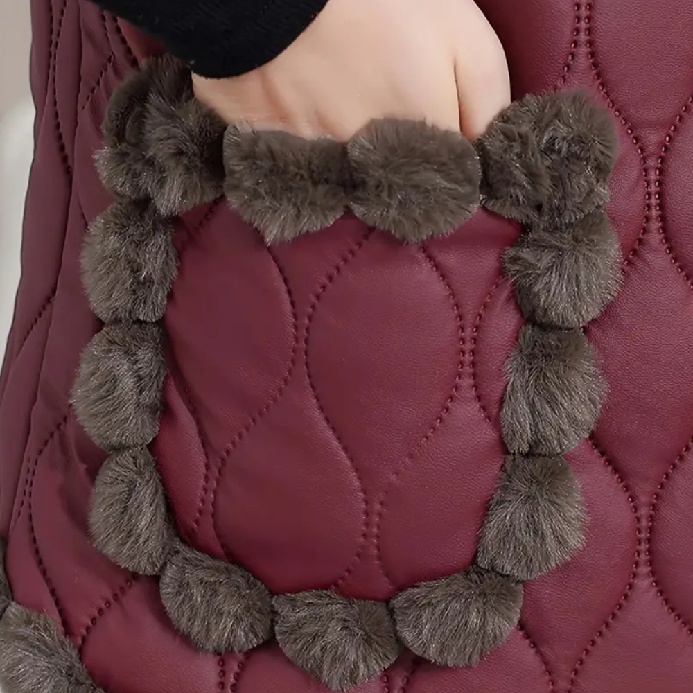 Hand in een bordeauxrode gewatteerde jaszak met grijze pluche pompons, wintermode, warme kleding, stijlvolle jasdetails.