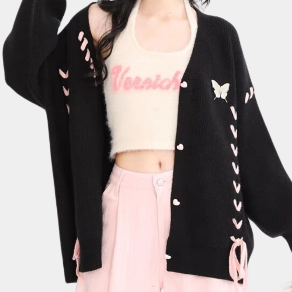Zwarte cardigan met roze details en vlinderapplicatie, gedragen over een witte top met roze tekst. Modieuze dameskleding, trendy herfstoutfit.