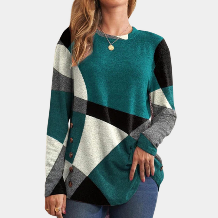 Vrouw draagt een Emery dames T-shirt met lange mouwen, geometrisch patroon in groen, zwart en wit, knoopdetails aan de zijkant. Modieuze dameskleding.
