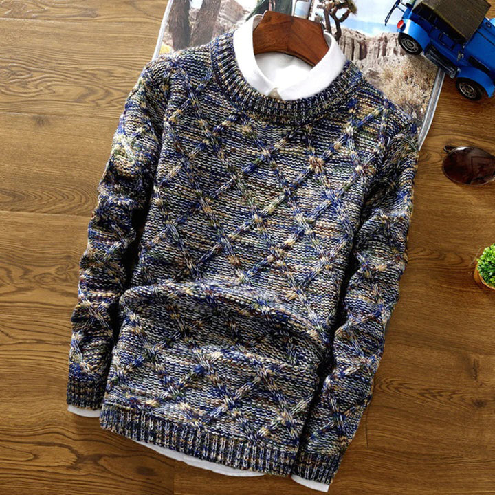 Grofgebreide herentrui in blauw en grijstinten, met een geruit patroon, op een houten vloer. Perfect voor wintermode en casual herenkleding.