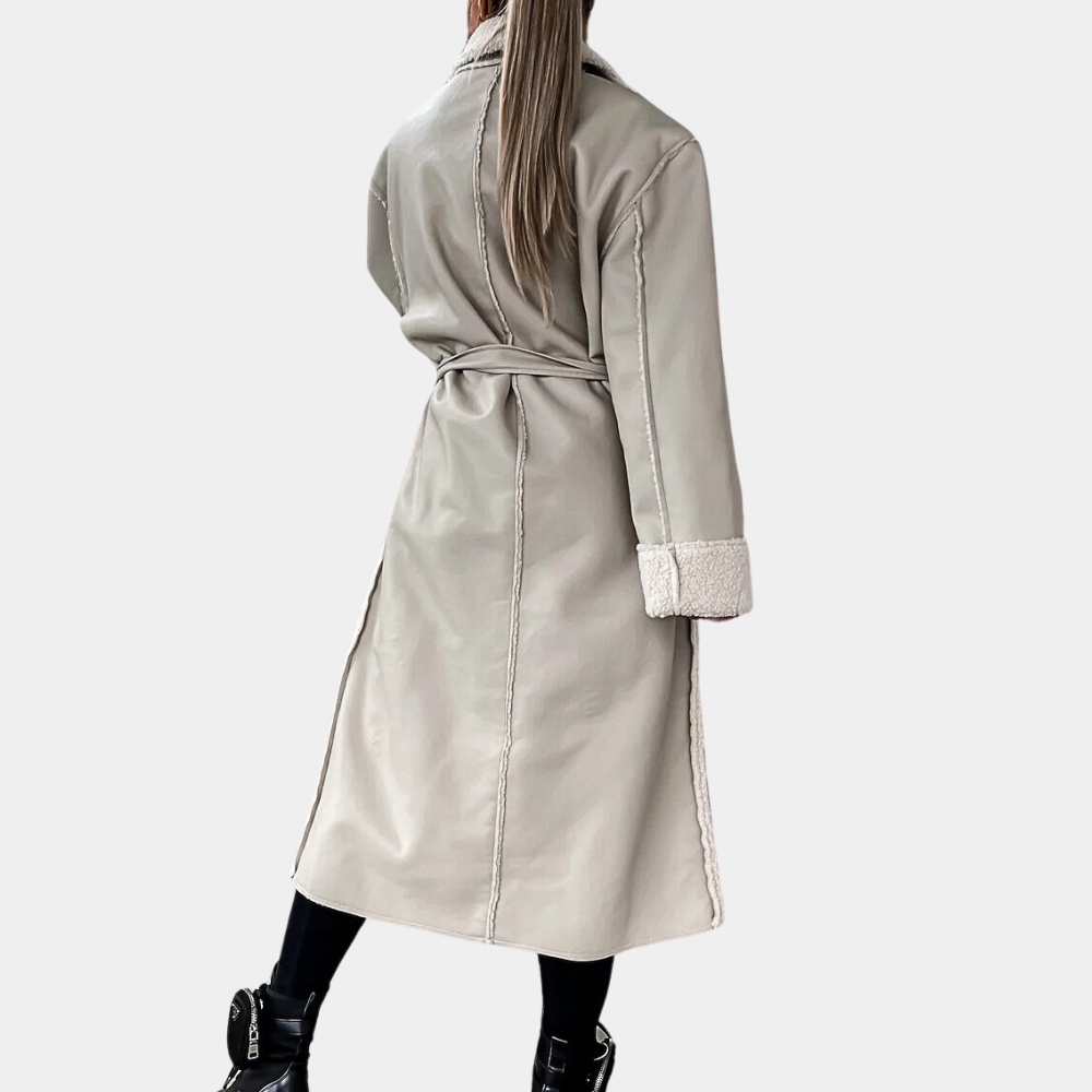 Vrouw in lange beige trenchcoat met ceintuur, zwarte laarzen; stijlvolle wintermode, trendy dameskleding, elegante jas, achteraanzicht.