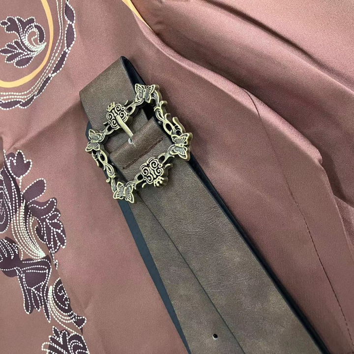 Bruine leren riem met sierlijke metalen gesp op een decoratieve achtergrond. Stijlvolle herenaccessoire, perfect voor modieuze outfits.