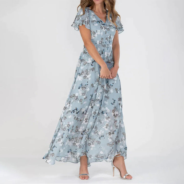 Vrouw in lange bloemenjurk, lichtblauw met korte mouwen, elegante zomerjurk voor dames, perfect voor bruiloften en speciale gelegenheden.