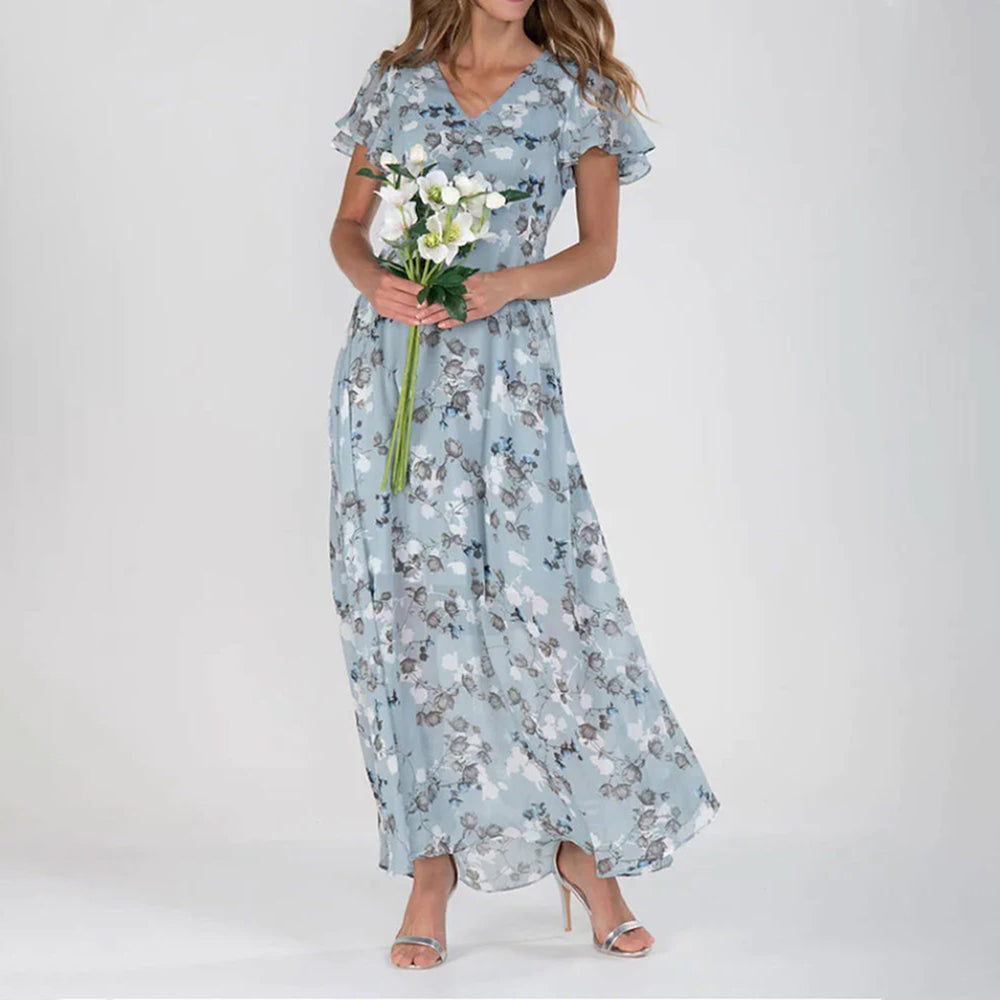Vrouw in lange blauwe bloemenjurk met korte mouwen, houdt een boeket witte bloemen vast. Perfecte damesjurk voor lente en zomer.