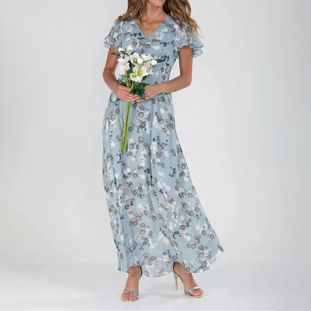 Vrouw in lange blauwe bloemenjurk met korte mouwen, houdt een boeket witte bloemen vast. Perfecte damesjurk voor lente en zomer.