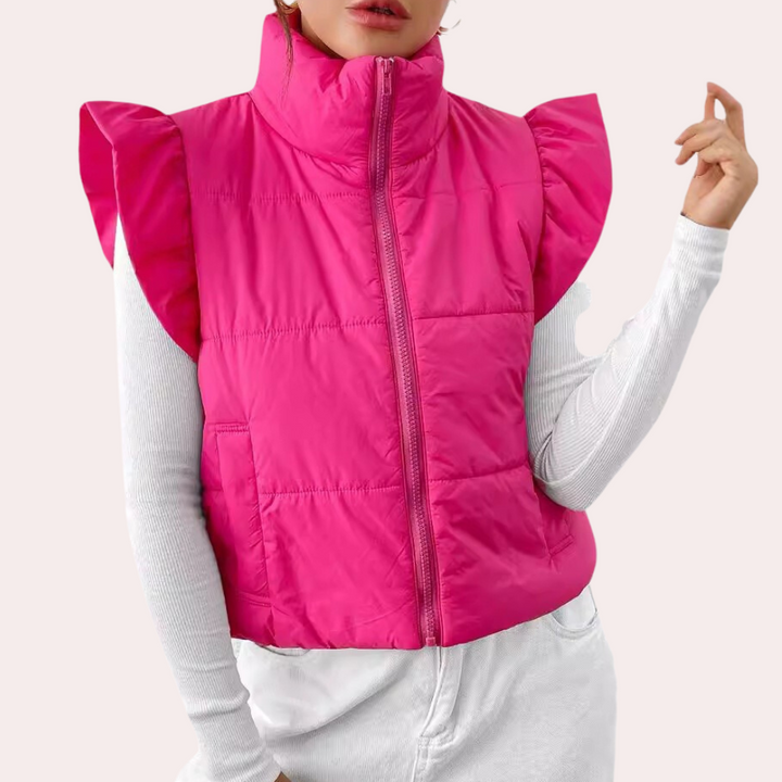 Roze gewatteerd dames bodywarmer met rits en ruches, gedragen over een witte trui. Modieuze winterkleding, trendy en comfortabel.
