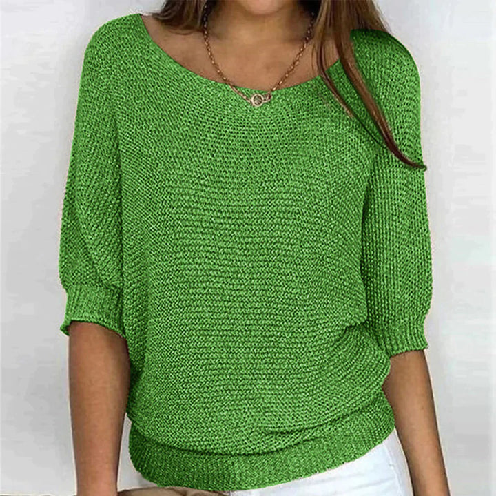 Vrouw draagt groene gebreide trui met driekwart mouwen, ronde hals en witte broek. Trendy damesmode, casual stijl, comfortabele kleding.