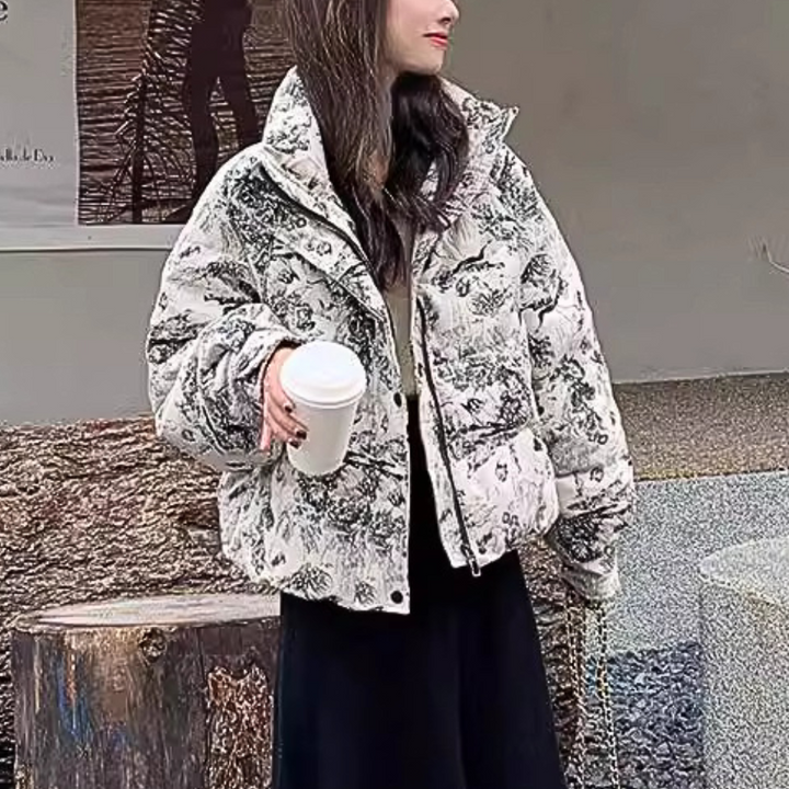 Vrouw in modieuze gewatteerde jas met bloemenprint, houdt een koffiebeker vast. Trendy winterkleding, casual stijl, buitenomgeving.