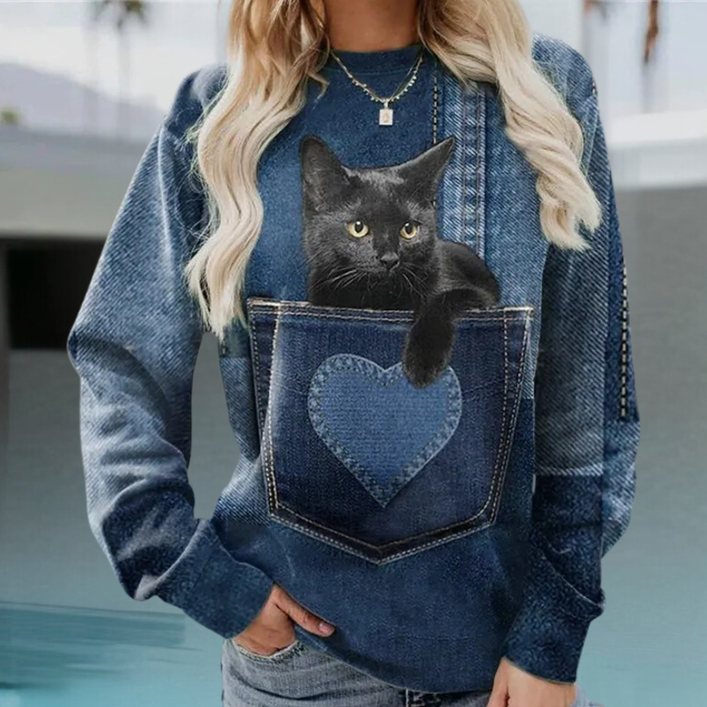 Vrouw in denim trui met zwarte kat in hartvormige zak, casual mode, trendy kleding, kattenliefhebber outfit, stijlvolle damestrui.