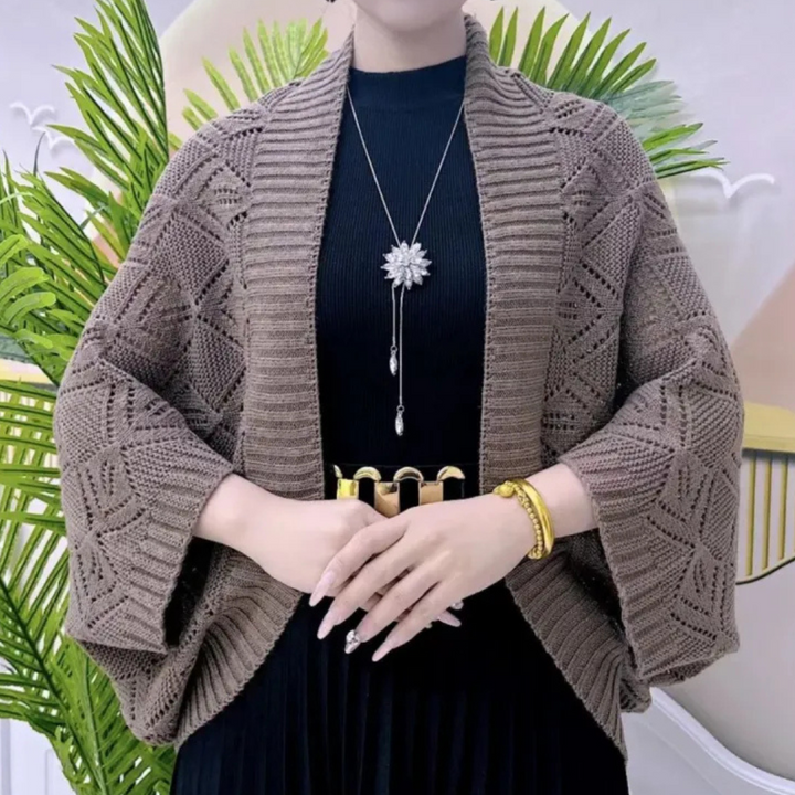 Vrouw draagt gebreid bruin vest met patroon, zwarte jurk en gouden riem. Accessoires: lange ketting met bloemhanger, gouden armband.