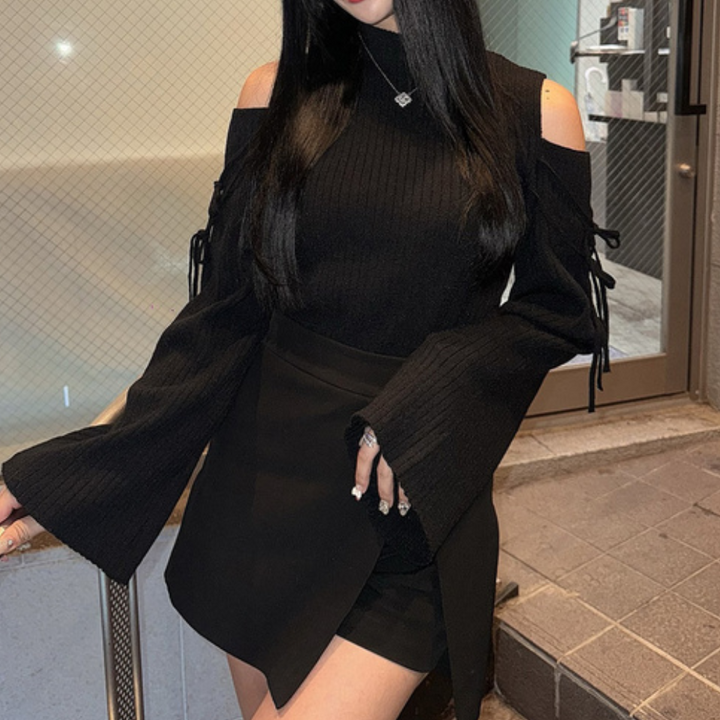 Vrouw in zwarte off-shoulder trui met wijde mouwen en zwarte rok, modieuze herfstoutfit, stedelijke achtergrond, trendy dameskleding.