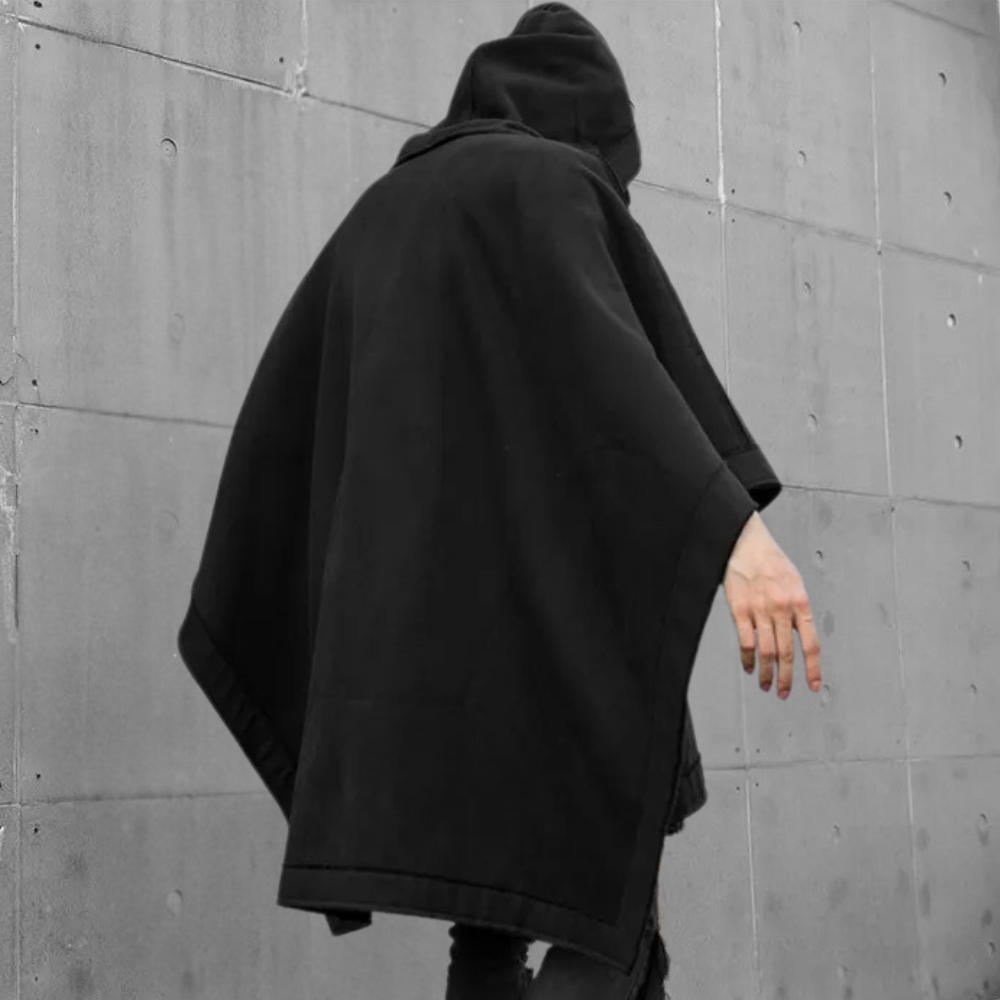 Zwarte hoodie cape, minimalistisch design, urban streetwear, unisex mode, grijze betonnen achtergrond, moderne stijl, casual kleding.