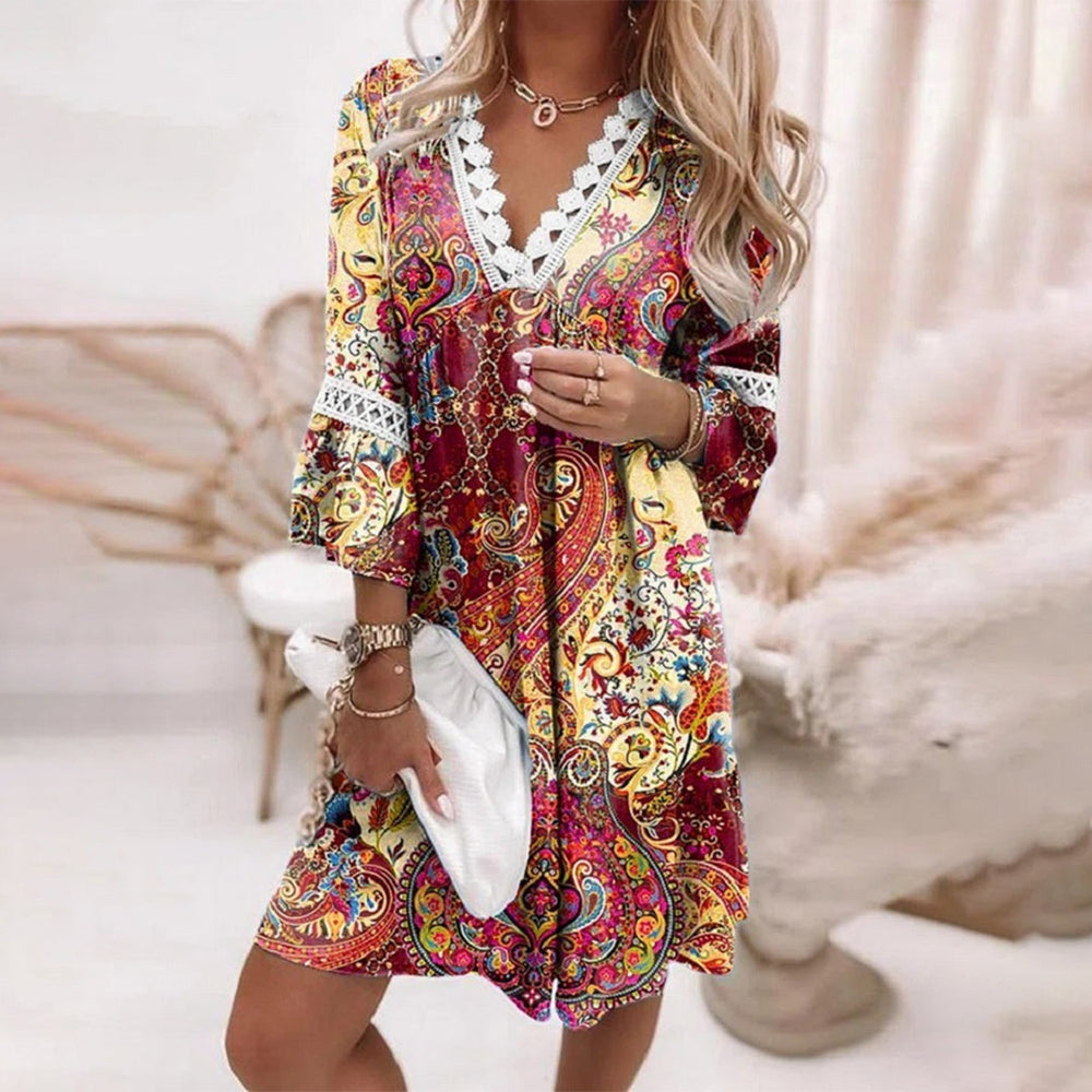 Vrouw in kleurrijke zomerjurk met paisley-patroon en kanten details, houdt witte clutch vast. Perfecte outfit voor zomerse gelegenheden.