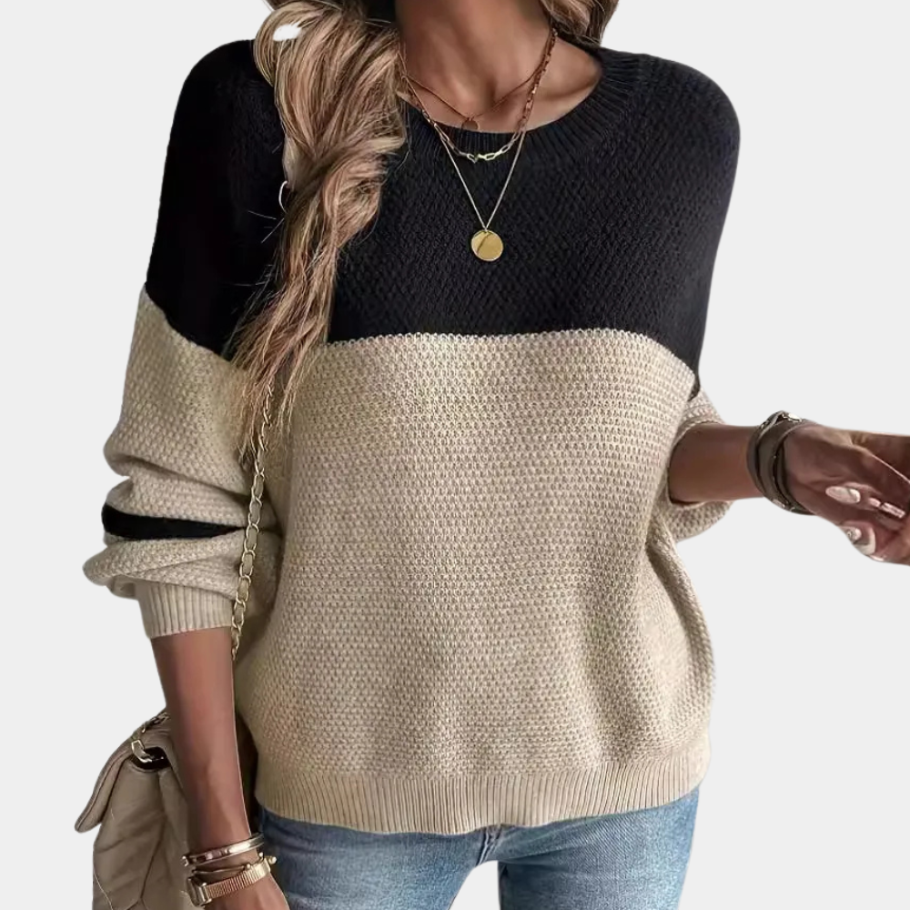Vrouw draagt stijlvolle zwart-beige trui met ronde hals, gecombineerd met blauwe jeans en gouden sieraden. Perfecte herfstmode voor dames.