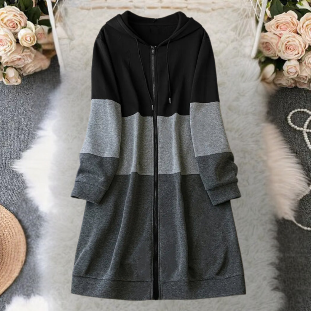 Zwart-grijze colorblock hoodie jurk met rits, lange mouwen en capuchon, liggend op een witte pluizige achtergrond met bloemen en hoed.
