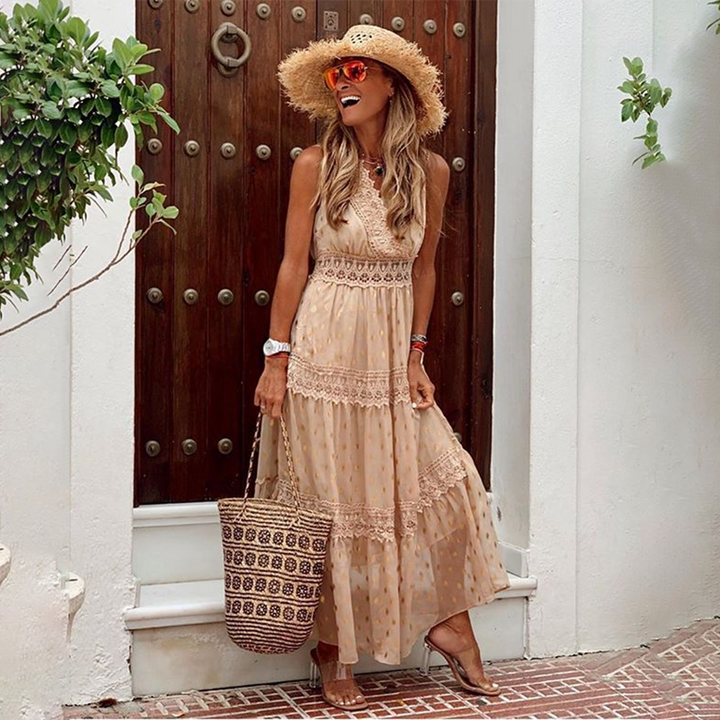 Vrouw in beige maxi-jurk met kant, strohoed en zonnebril, poseert voor houten deur. Zomerse outfit, boho-stijl, perfect voor strandvakantie.