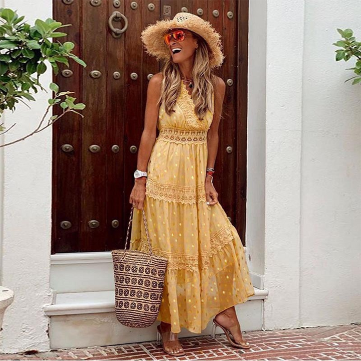 Vrouw in gele maxi-jurk met stippen en kanten details, draagt een strohoed en zonnebril, poseert voor houten deur. Zomerse mode, dameskleding.