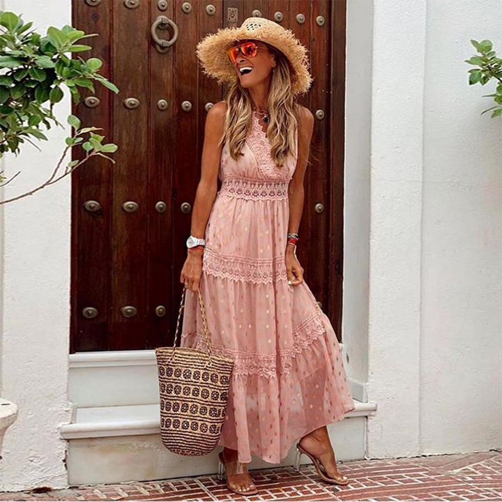 Vrouw in roze maxi-jurk met stippen, strohoed en zonnebril, poseert voor houten deur. Zomerse outfit, boho-stijl, strandtas.