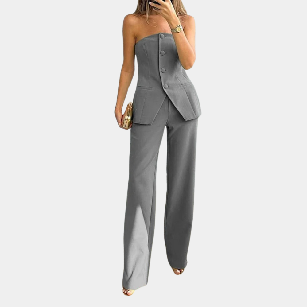 Vrouw in grijs strapless damespak met wijde pijpen, gouden clutch en horloge. Elegante mode, trendy dameskleding, stijlvolle outfit.