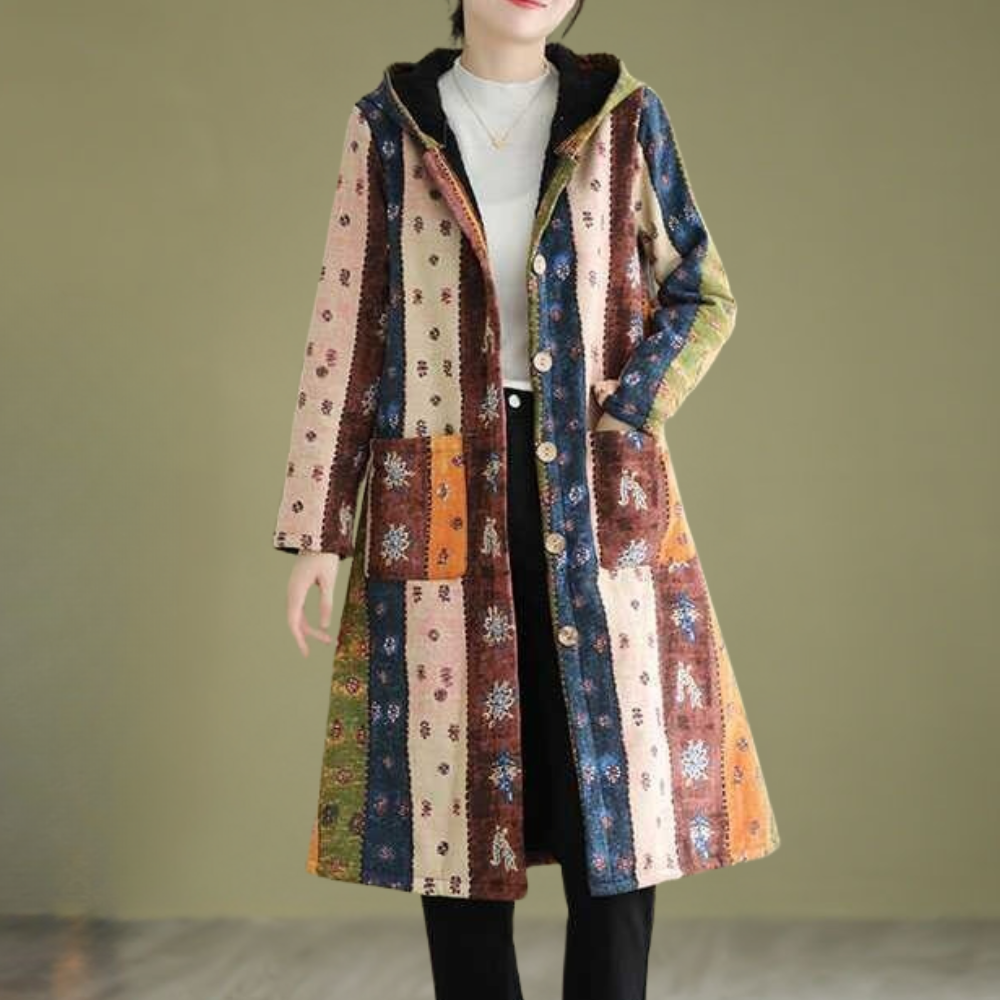 Vrouw draagt lange, kleurrijke patchwork jas met capuchon en knopen, bohemian stijl, tegen olijfgroene achtergrond. Modieuze dameskleding herfst.