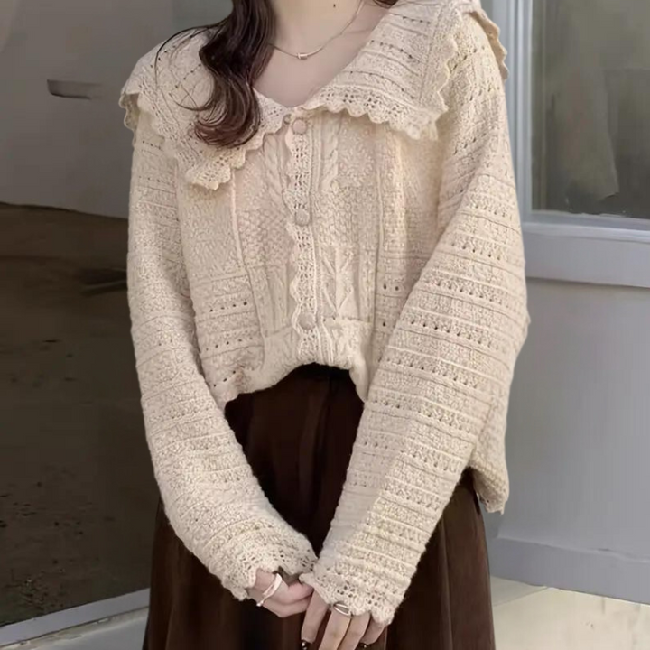 Vrouw in crèmekleurige gebreide trui met kanten kraag, lange mouwen en knoopsluiting, staand voor een neutrale achtergrond. Trendy herfstmode.