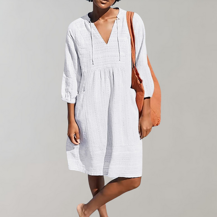 Vrouw in witte zomerjurk met V-hals en driekwartsmouwen, draagt een oranje tas. Perfecte damesjurk voor casual zomermode.