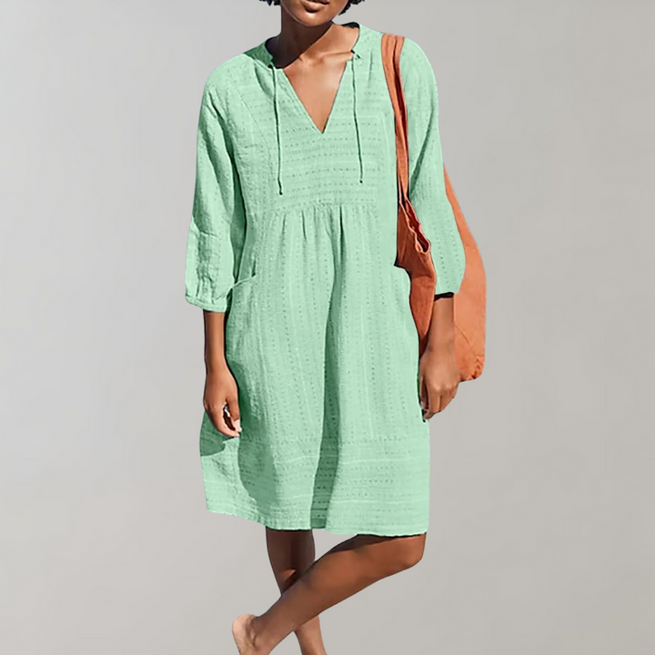 Vrouw in mintgroene zomerjurk met V-hals en driekwartsmouwen, draagt een oranje tas. Perfecte casual outfit voor dames.