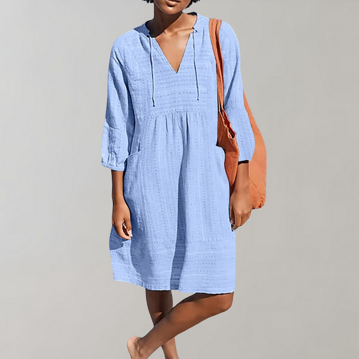 Vrouw in lichtblauwe zomerjurk met V-hals en driekwart mouwen, draagt een oranje tas. Perfecte casual outfit voor dames.