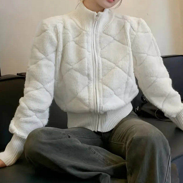 Vrouw draagt witte gewatteerde jas met ruitpatroon, zittend op zwarte bank. Modieuze winterkleding, trendy damesjas, comfortabele outfit.