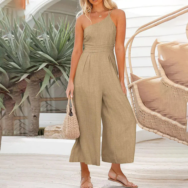 Vrouw in stijlvolle kaki jumpsuit met asymmetrische halslijn, draagt een gevlochten tas. Perfecte zomeroutfit, casual en elegant.