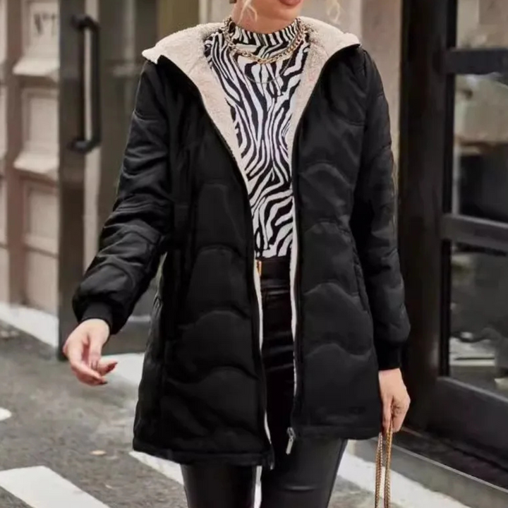 Zwarte gewatteerde winterjas met capuchon, gedragen door vrouw met zebraprint trui en leren broek, modieuze straatstijl, herfst-winter mode.