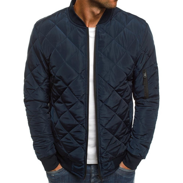 Donkerblauwe gewatteerde bomberjack voor heren, met ritszak op de mouw. Stijlvolle herenjassen, wintermode, casual outfit.