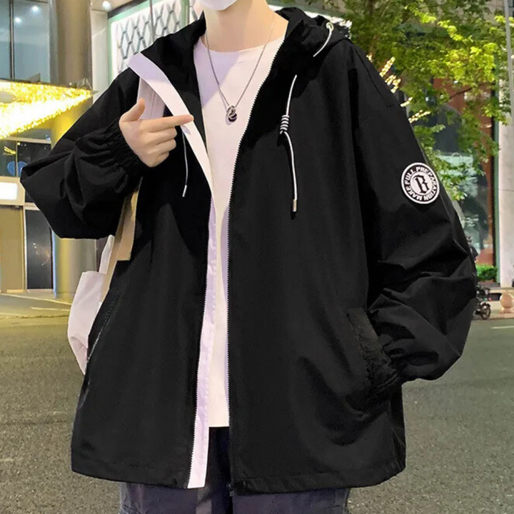 Zwarte unisex windjack met capuchon, ritssluiting en embleem op mouw. Casual streetwear, ideaal voor herfst en lente. Comfortabele pasvorm.