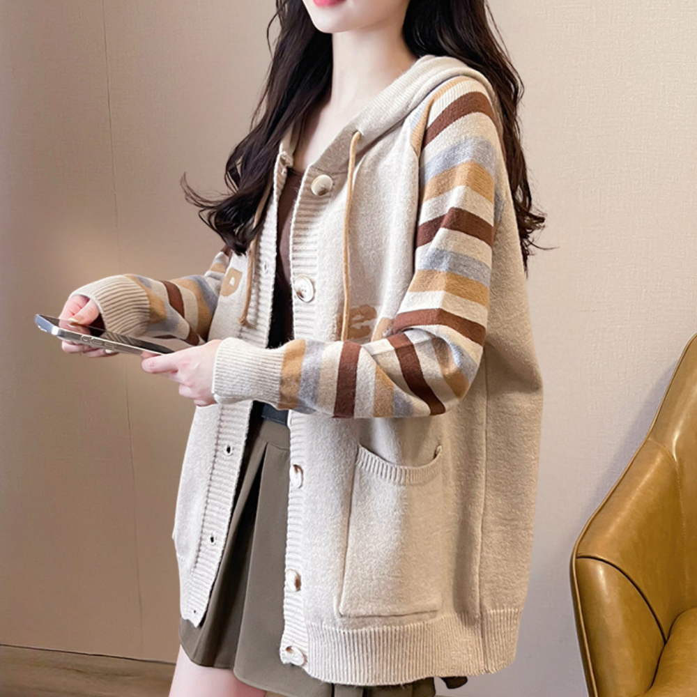 Vrouw in beige gebreid vest met capuchon en gestreepte mouwen, bruine en beige tinten, casual herfstmode, smartphone in hand.