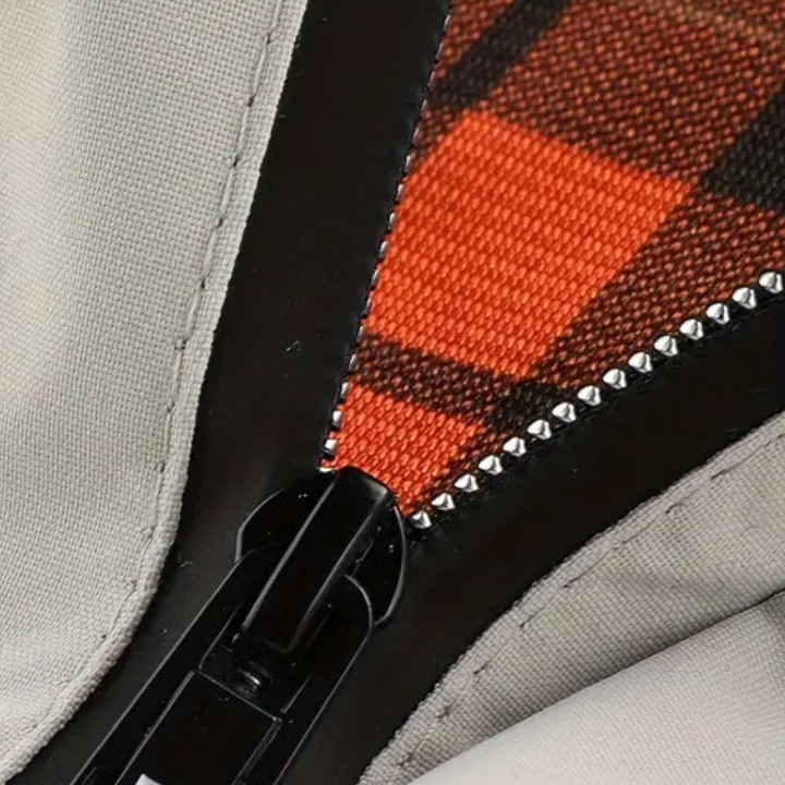 Close-up van een zwarte ritssluiting op een beige stof met oranje geruit patroon. Modieuze ritssluiting, textiel, kledingaccessoire.