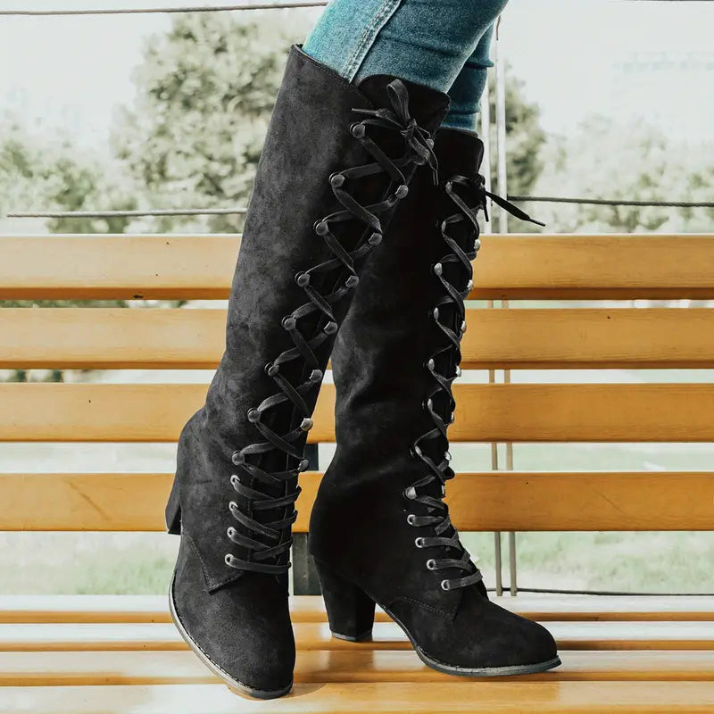 Zwarte suède laarzen met veterdetail en blokhak, gedragen door persoon in blauwe jeans, op houten bank. Stijlvolle damesmode, herfst/winter schoenen.