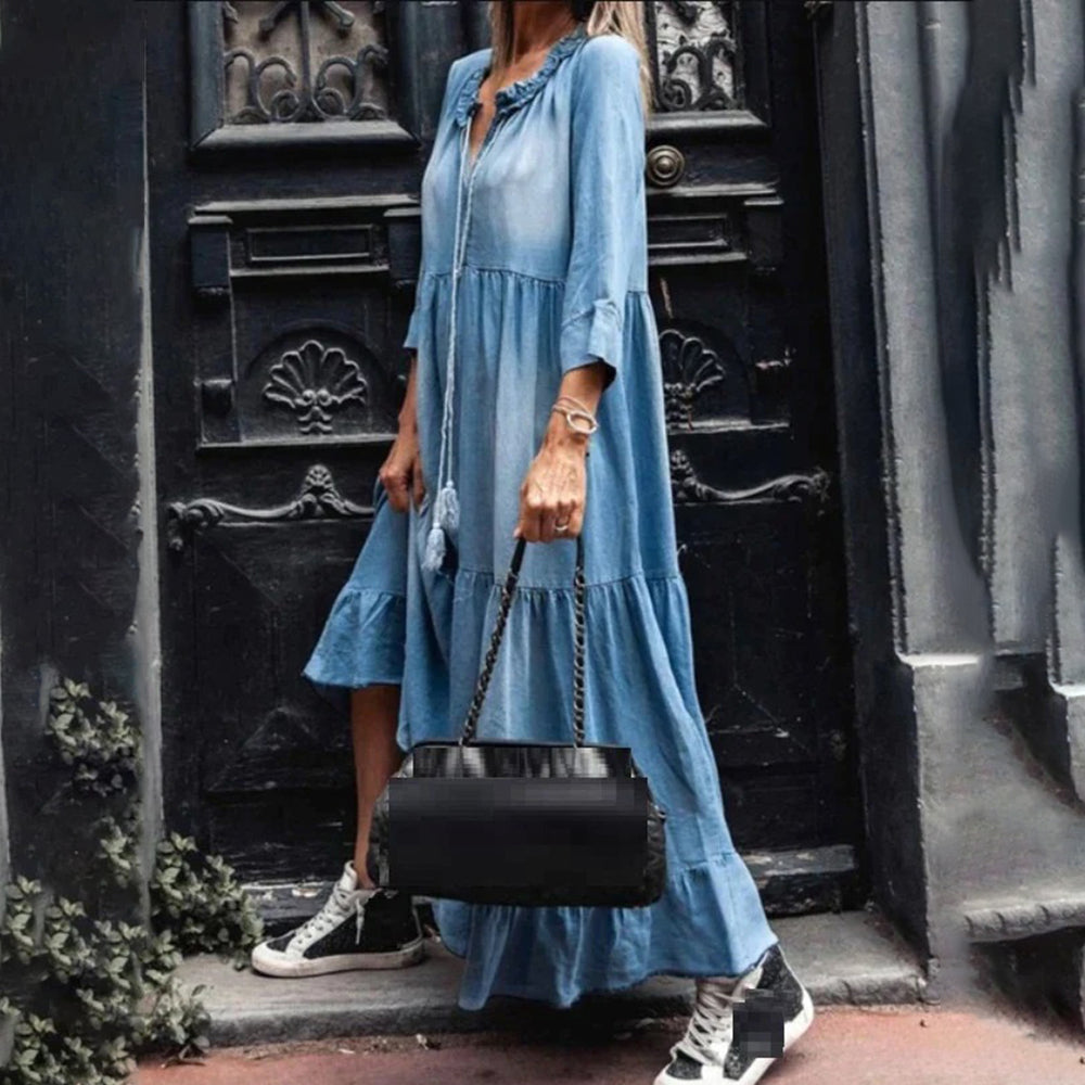 Vrouw in lichtblauwe maxi-jurk met sneakers voor antieke deur. Trendy mode, casual stijl, denim look, stedelijke achtergrond.