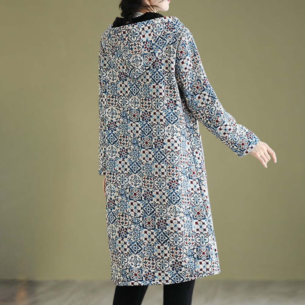 Vrouw in lange, kleurrijke jas met geometrisch patroon, staand tegen een effen achtergrond. Modieuze dameskleding, herfst-winter stijl.