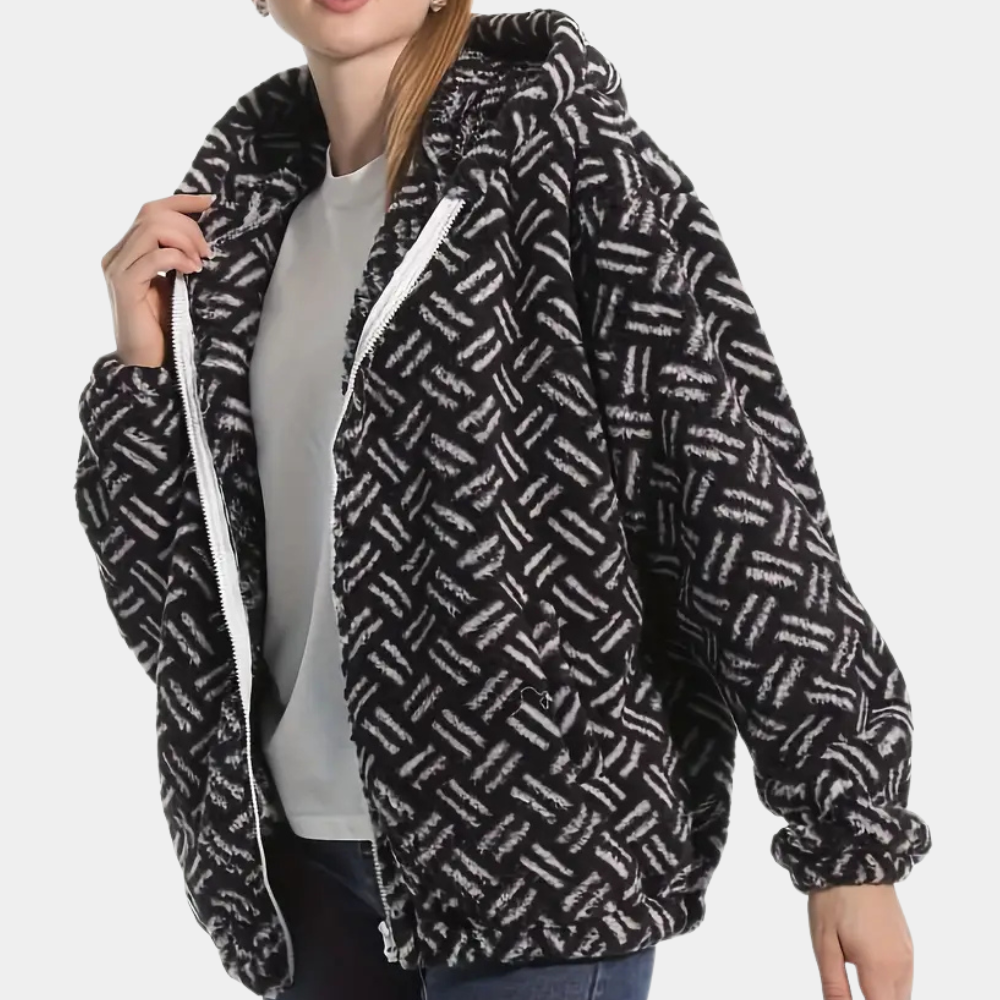 Vrouw draagt zwarte fleece jas met wit geometrisch patroon, capuchon en ritssluiting. Modieuze winterkleding, comfortabele damesjas.