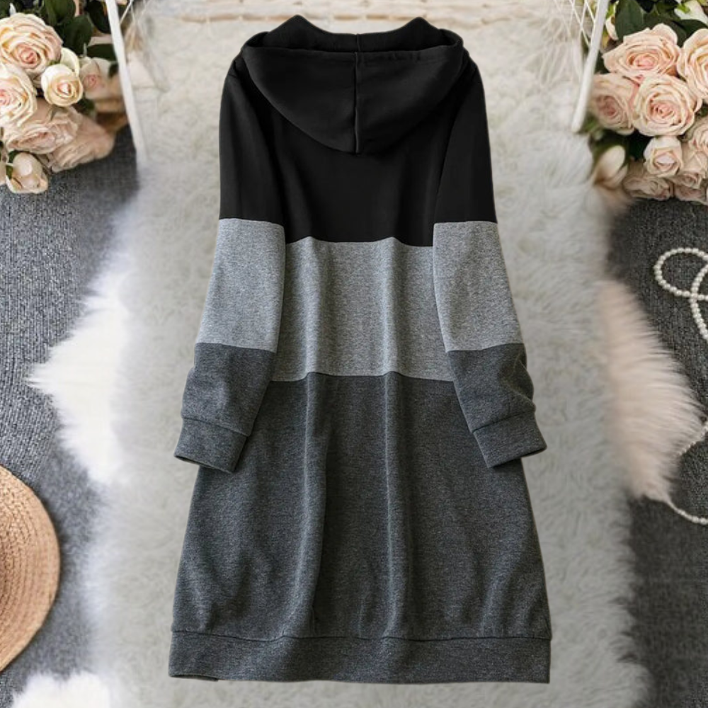 Zwart-grijze colorblock hoodie jurk op een witte vloerkleed achtergrond, omringd door bloemen. Comfortabele damesmode, casual stijl.