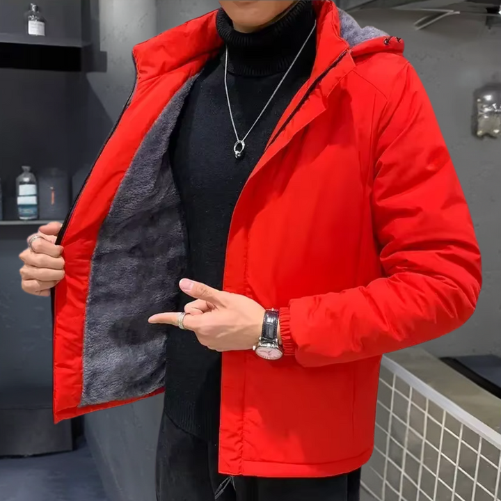 Man in rode winterjas met grijze voering, zwarte coltrui en zilveren ketting, wijst naar binnenkant van jas. Stijlvolle herenkleding, wintermode.